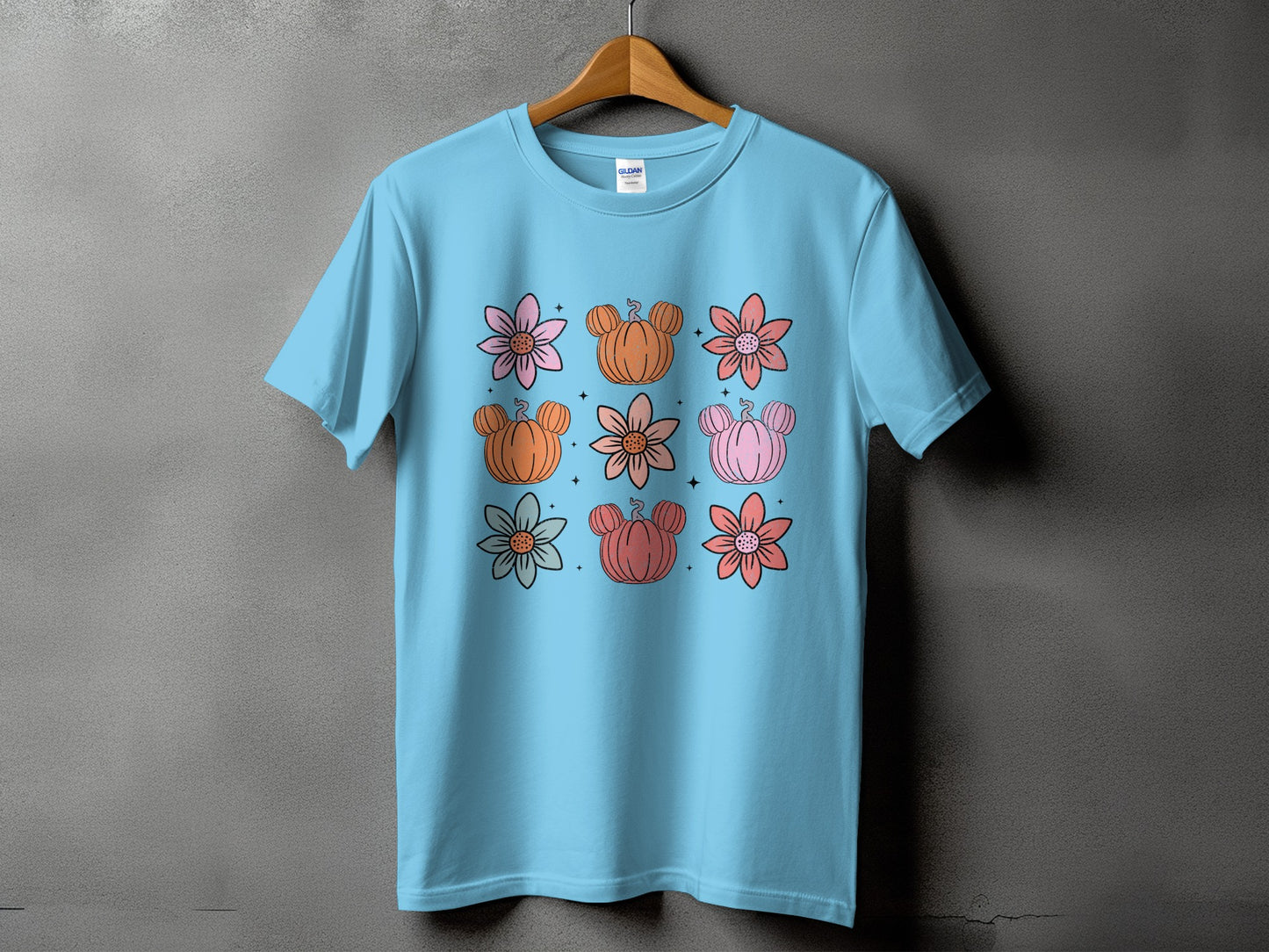 Light blue t-shirt with a grid of cartoon flowers and pumpkins with Mickey Mouse ears.