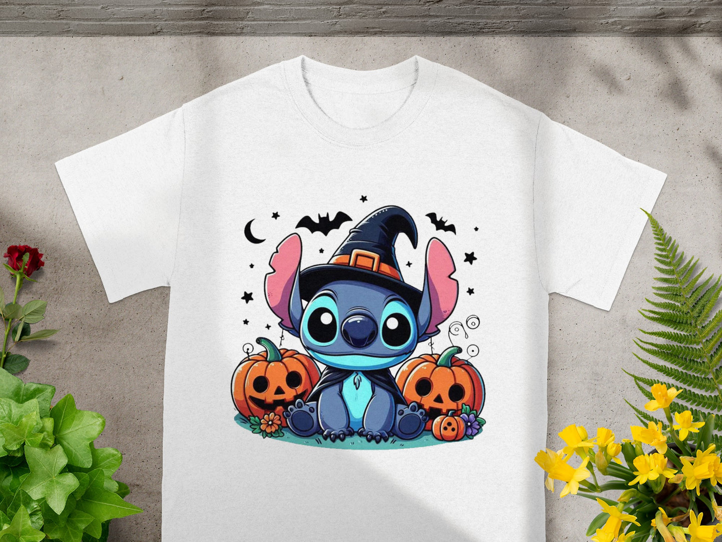 Stitch wearing a witch hat sits with Halloween pumpkins and bats on a white t-shirt.