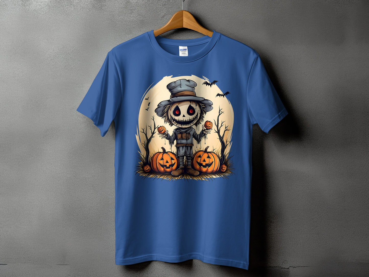 Blue t-shirt with a cartoon scarecrow holding pumpkins and bats against a moon.