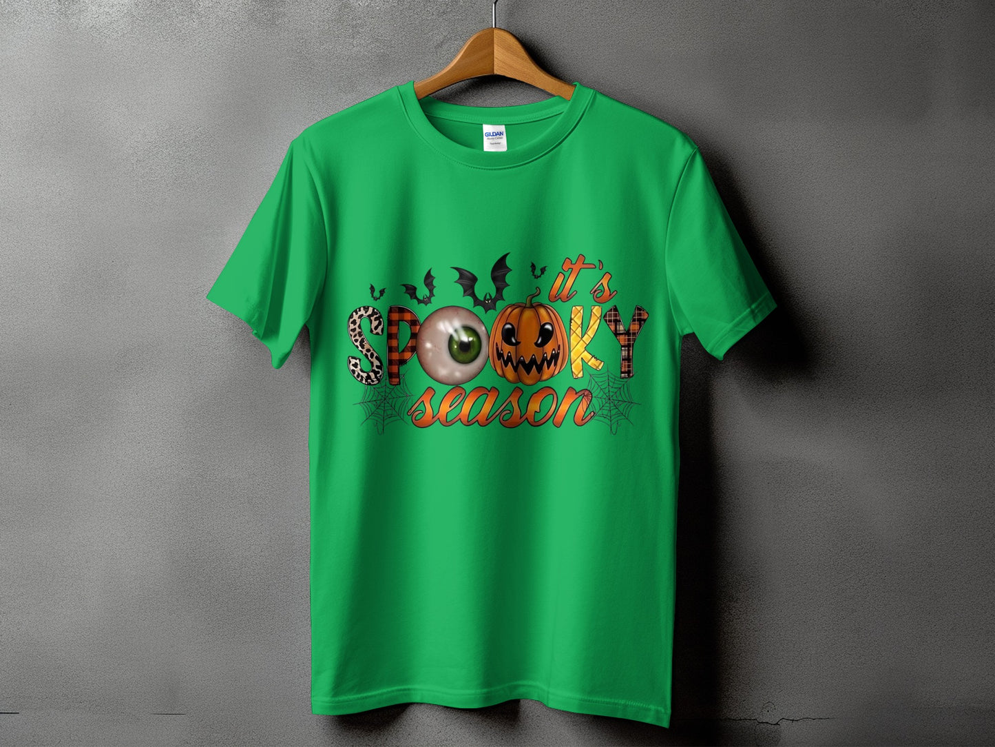 Green t-shirt with "It's Spooky Season" Halloween graphic featuring bats, eyeball, pumpkin, and spiderwebs.