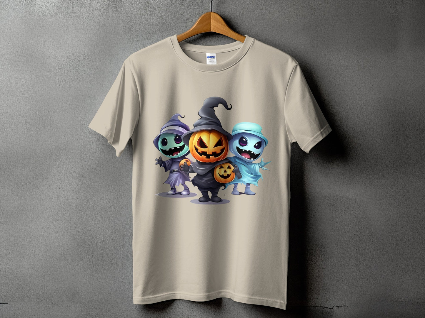 Light tan t-shirt with three cartoon Halloween characters: pumpkin, witch, and ghost.