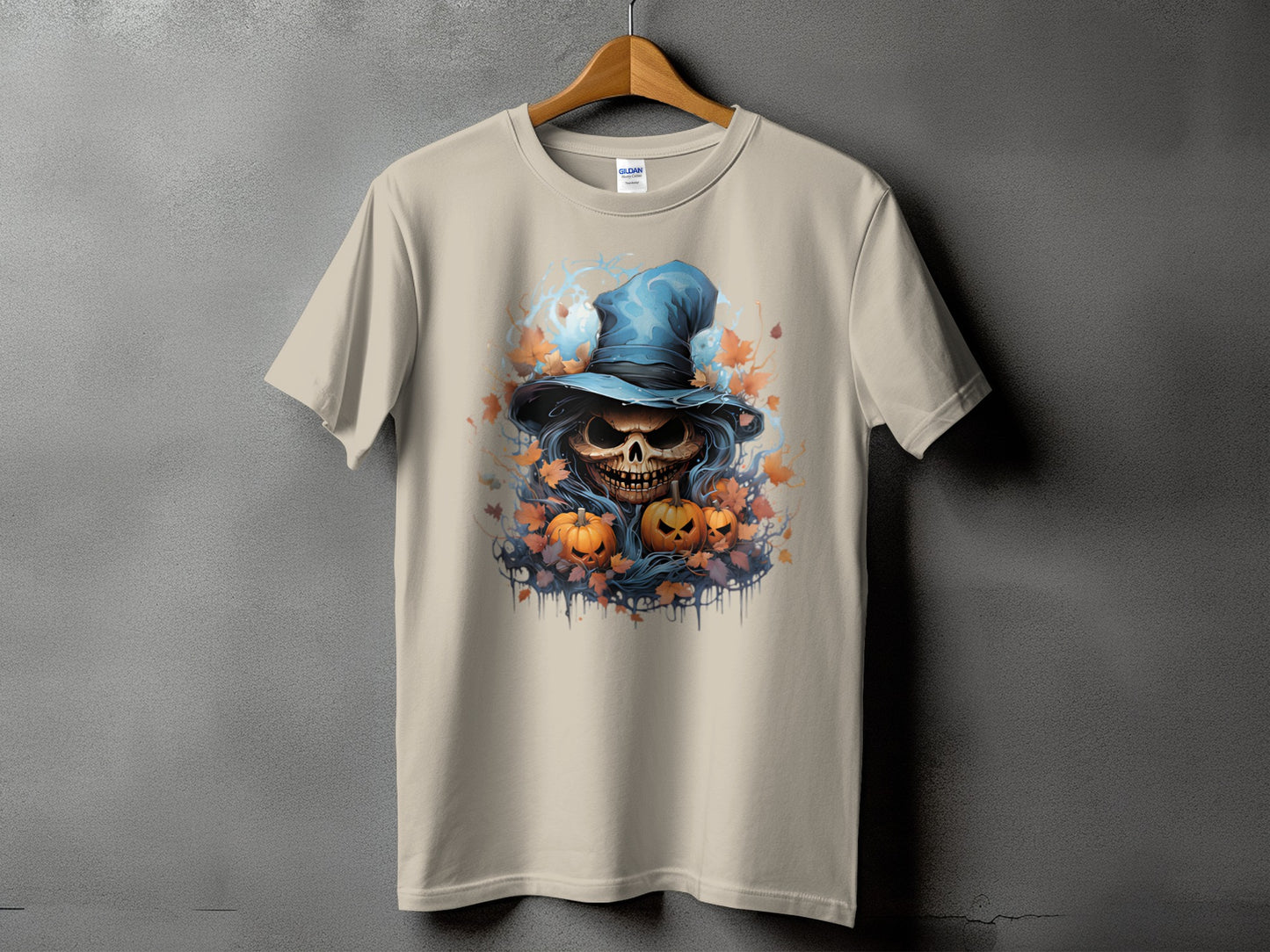 Skull in witch hat with pumpkins and fall leaves graphic on a tan t-shirt.