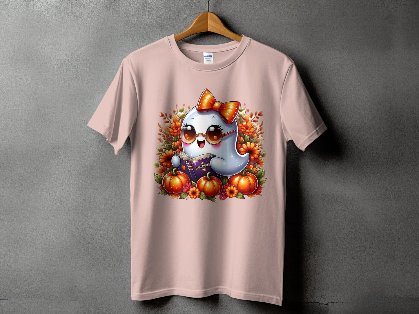 Pink t-shirt with cartoon ghost reading a book surrounded by pumpkins and flowers.