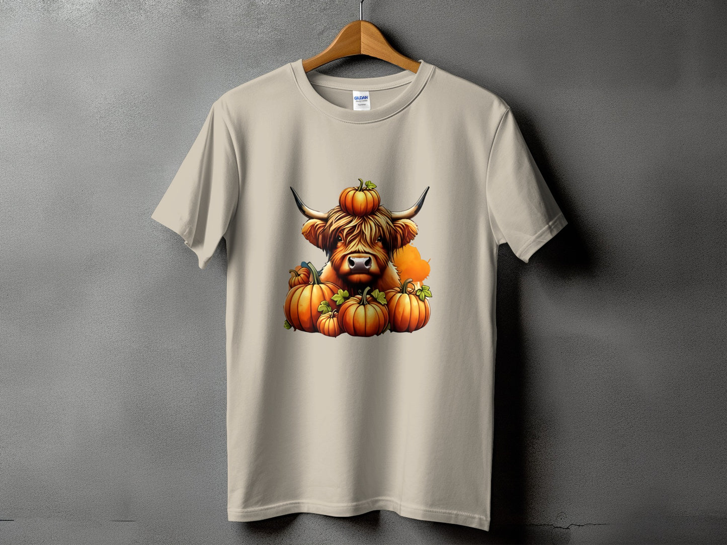 T-shirt with a Highland cow wearing a pumpkin on its head and surrounded by pumpkins.
