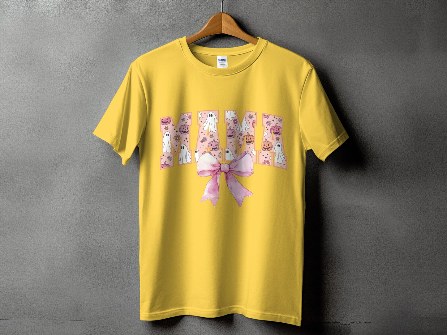 Yellow t-shirt with "Mama" text featuring ghosts, pumpkins, and flowers, with a pink bow.