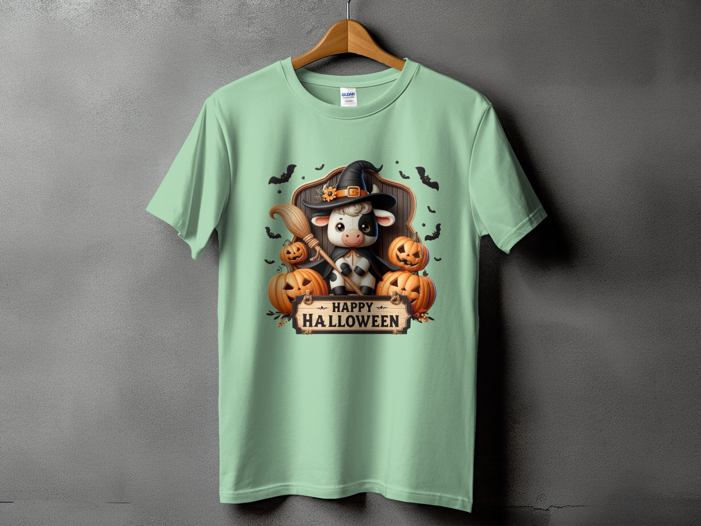 Light green t-shirt with a Halloween graphic featuring a cow in a witch hat and pumpkins.