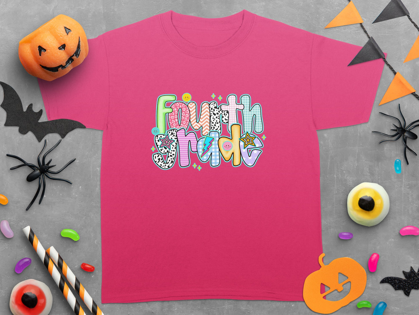 Pink t-shirt with "Fourth Grade" in colorful, textured font, surrounded by Halloween decorations.