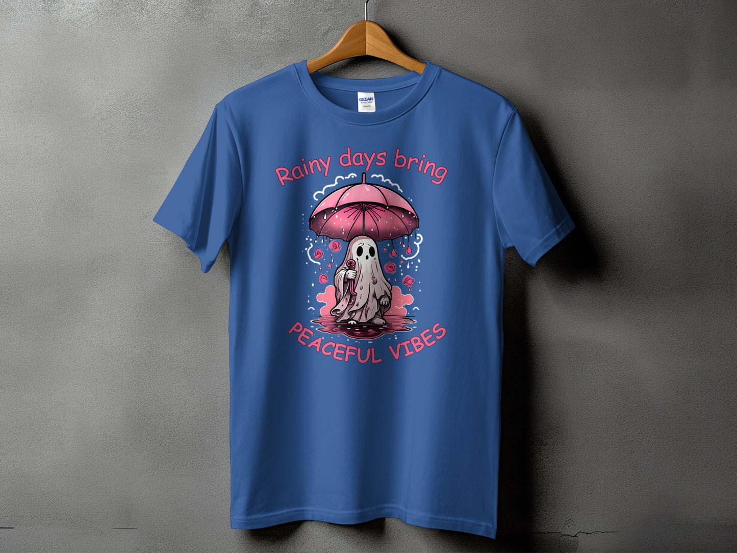 Blue t-shirt with a cartoon ghost under an umbrella, text "Rainy days bring peaceful vibes".