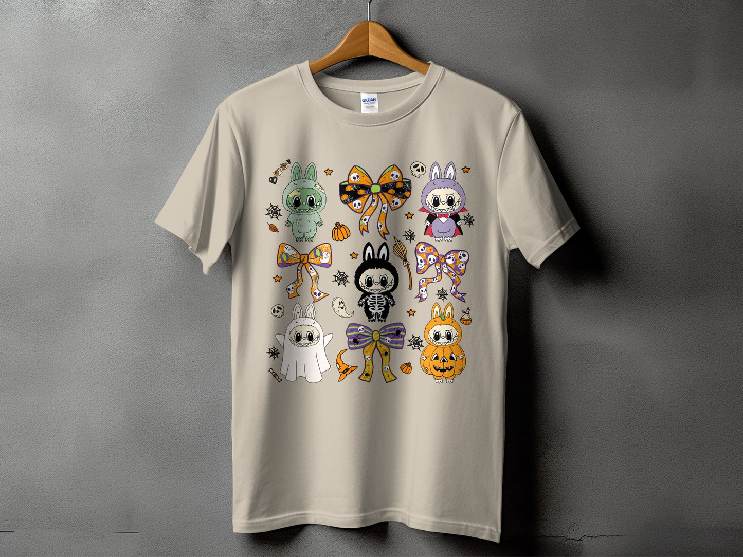 Light beige t-shirt with a repeating pattern of cute Halloween-themed cartoon characters and bows.
