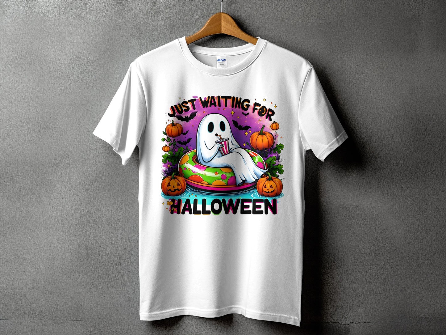 White t-shirt with a cartoon ghost on an inflatable ring surrounded by pumpkins, saying "Just Waiting for Halloween".
