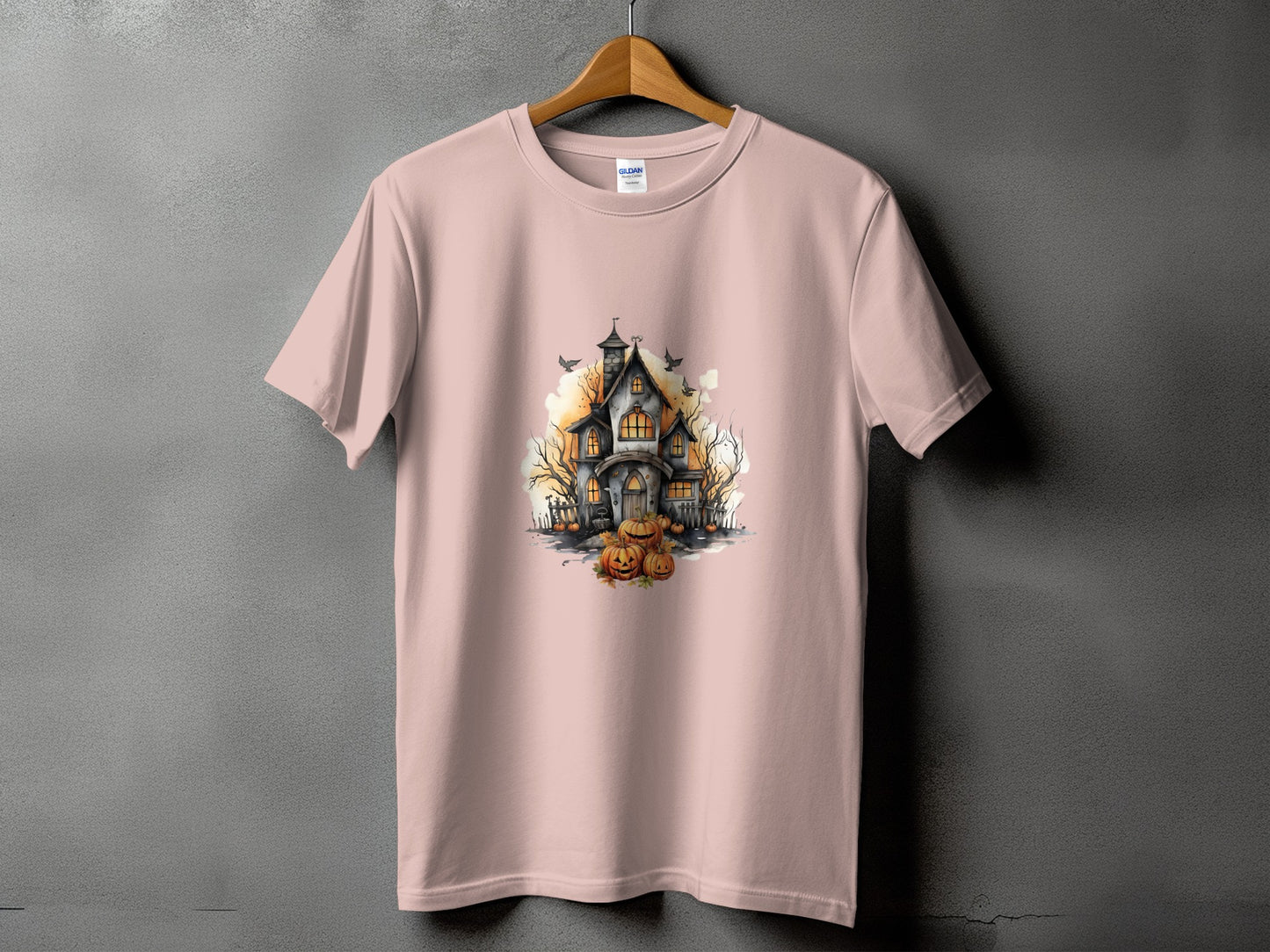 Pink t-shirt with a watercolor illustration of a haunted house and pumpkins.