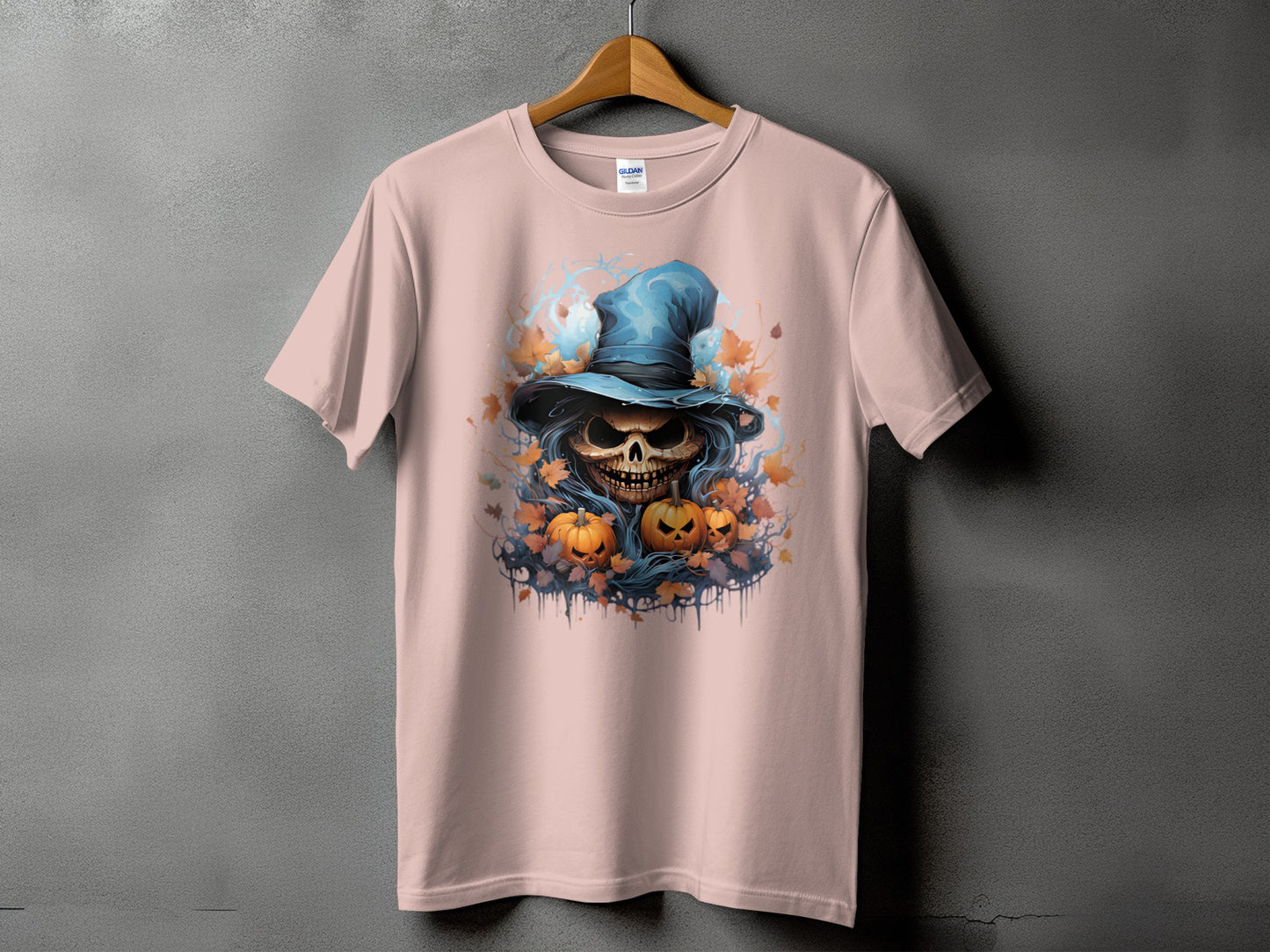 Pink t-shirt with a graphic of a skull wearing a blue hat surrounded by pumpkins and leaves.