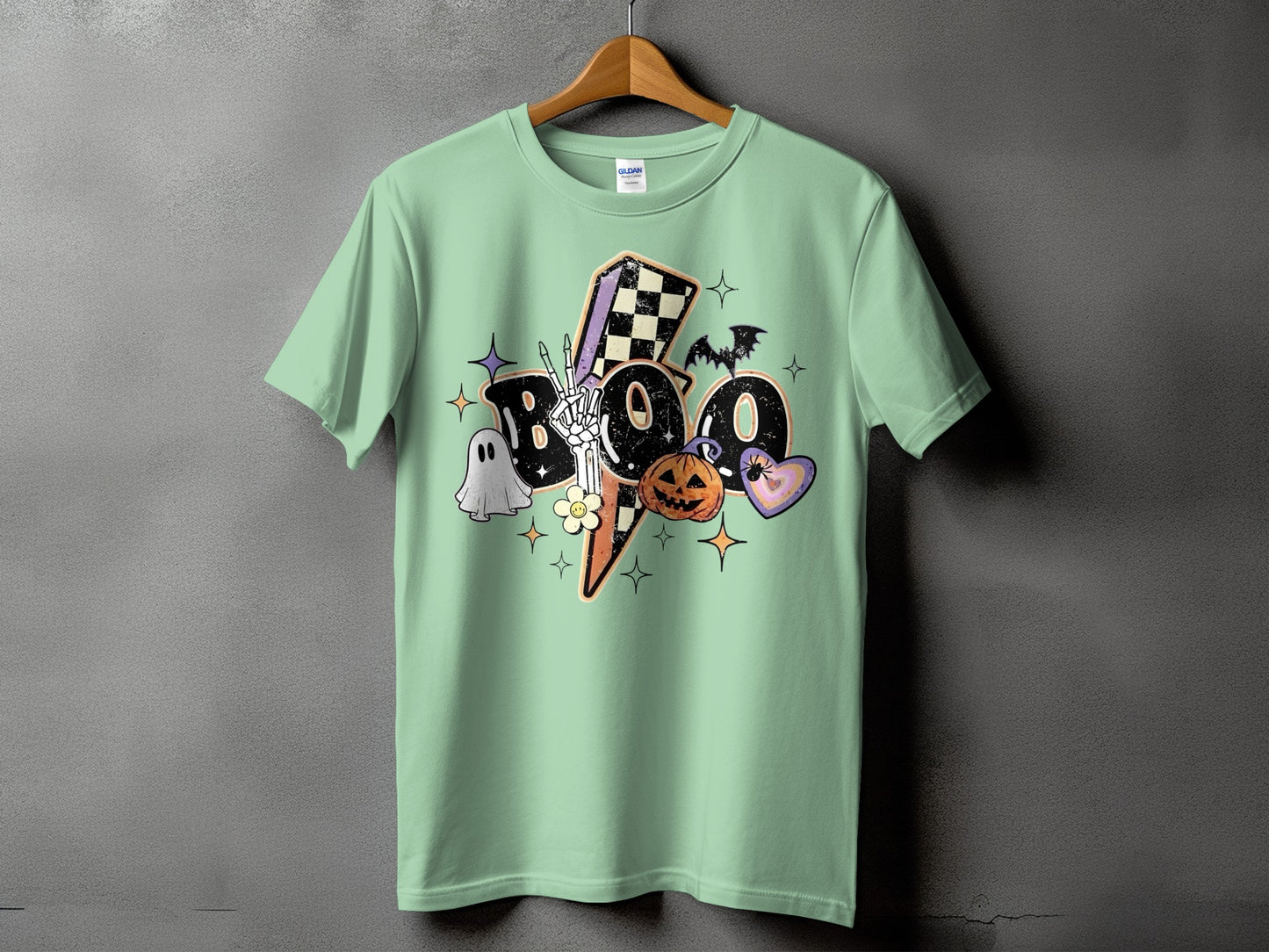 Light green t-shirt with "Boo" graphic featuring skeleton hand, ghost, pumpkin, and lightning bolt.