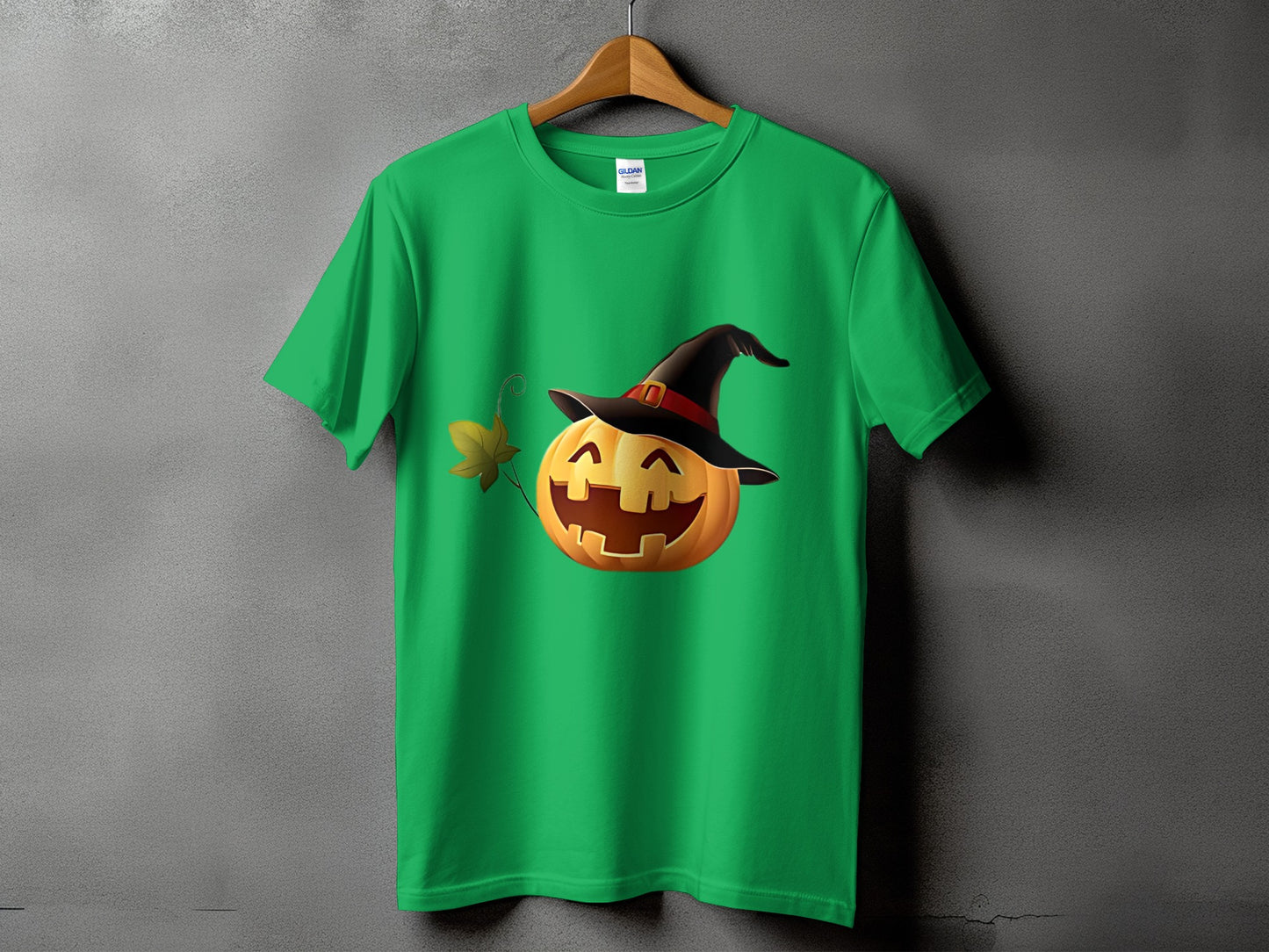 Green t-shirt with a smiling jack-o'-lantern wearing a witch hat and holding a leaf.