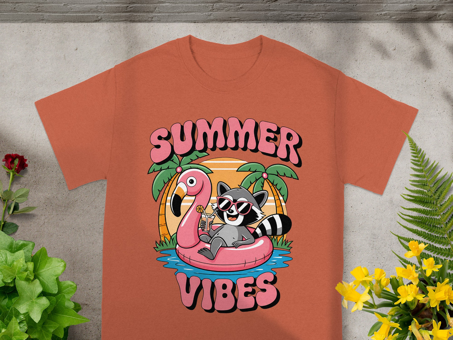 T-shirt graphic: Raccoon relaxing on flamingo float, "SUMMER VIBES" text.