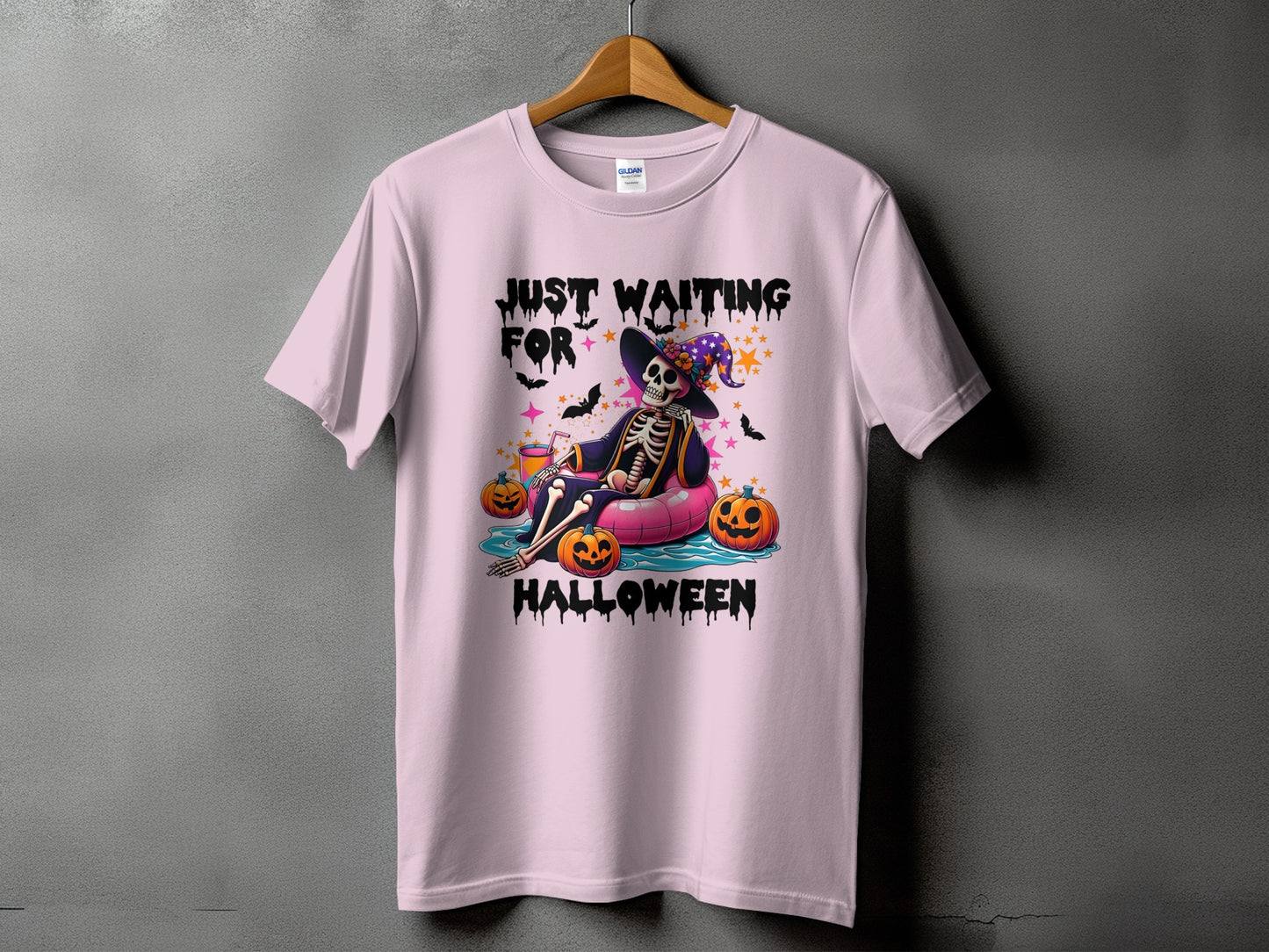 Light pink t-shirt with skeleton floating on a pink tube, text says "Just Waiting For Halloween".