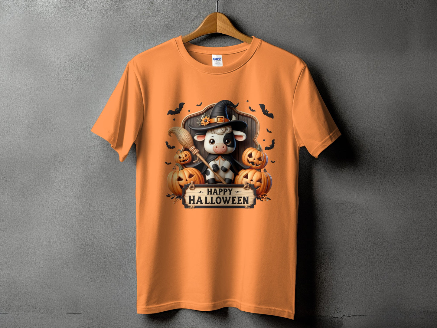 Orange t-shirt with a Halloween graphic of a cow in a witch hat with pumpkins and bats.