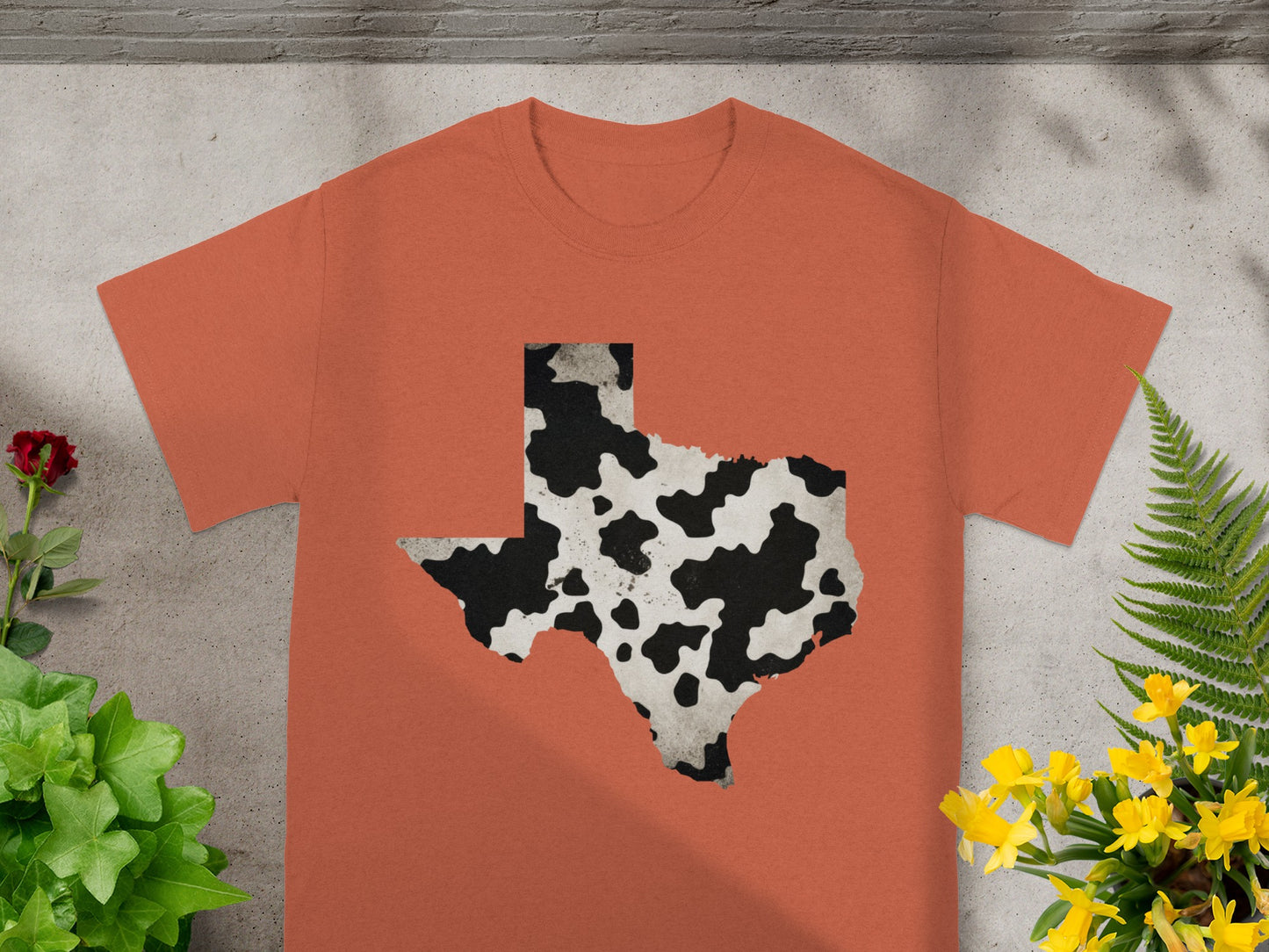 Orange t-shirt with a black and white cow print Texas state outline.