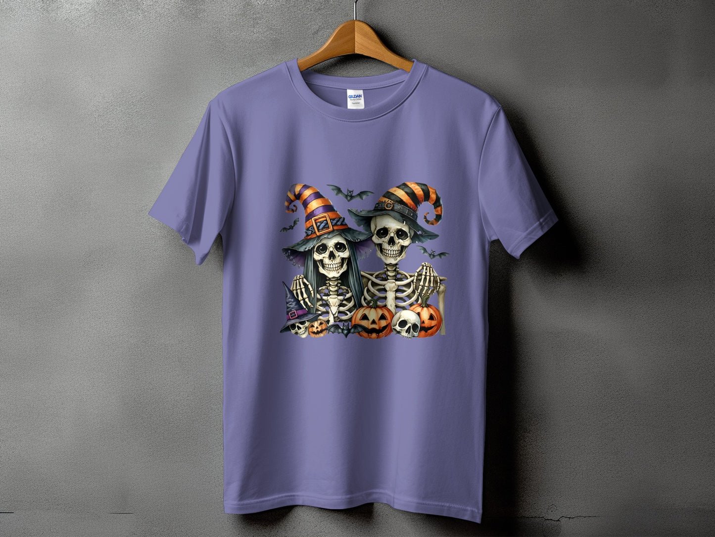 Two skeletons wearing witch hats with pumpkins and bats on a purple t-shirt.