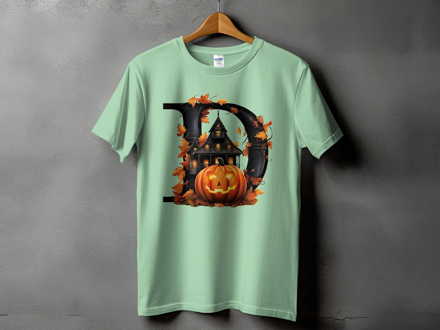 Light green t-shirt with a black letter D featuring a haunted house and jack-o'-lantern.