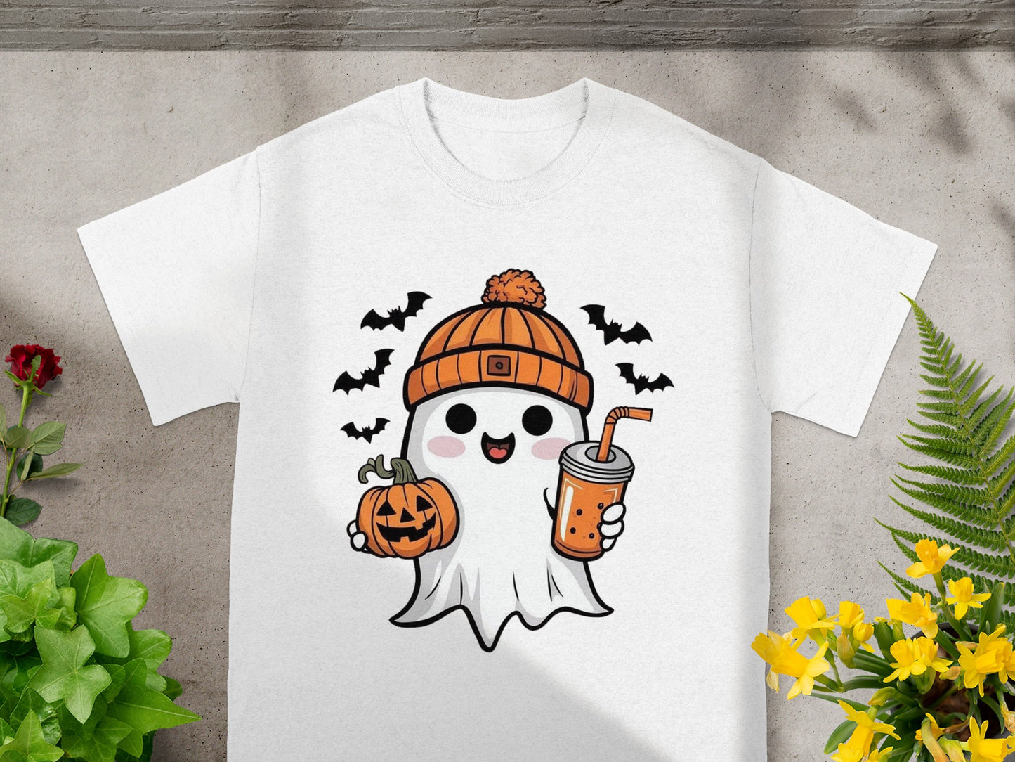 White t-shirt with a cartoon ghost holding a pumpkin and a drink, surrounded by bats.