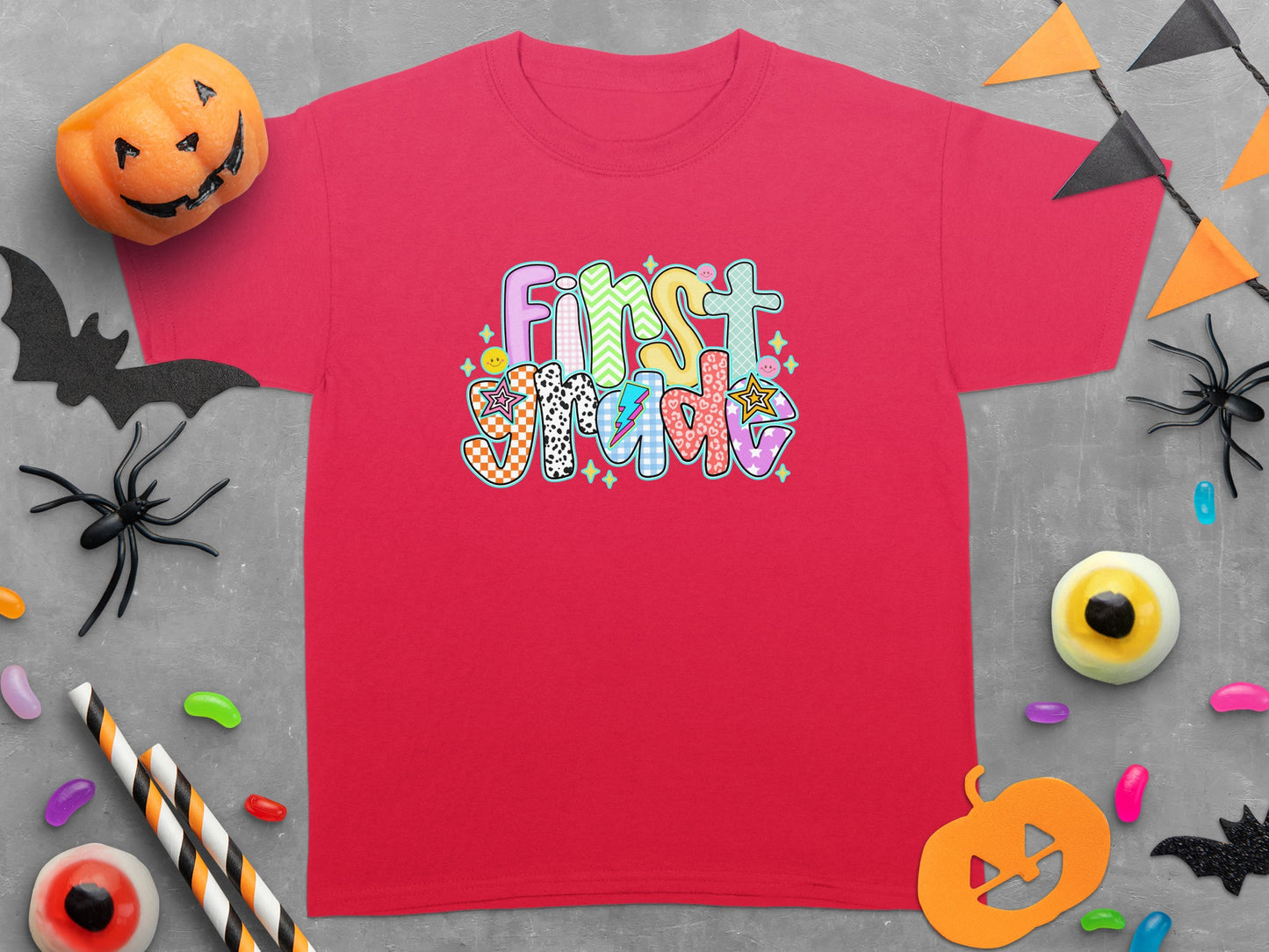 Red t-shirt with "First Grade" in colorful, patterned lettering and Halloween decorations.