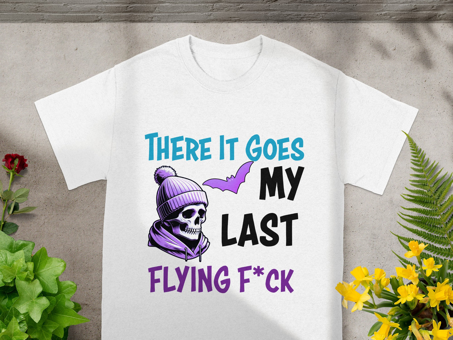 White t-shirt with purple skull in beanie and text "THERE IT GOES MY LAST FLYING F*CK".
