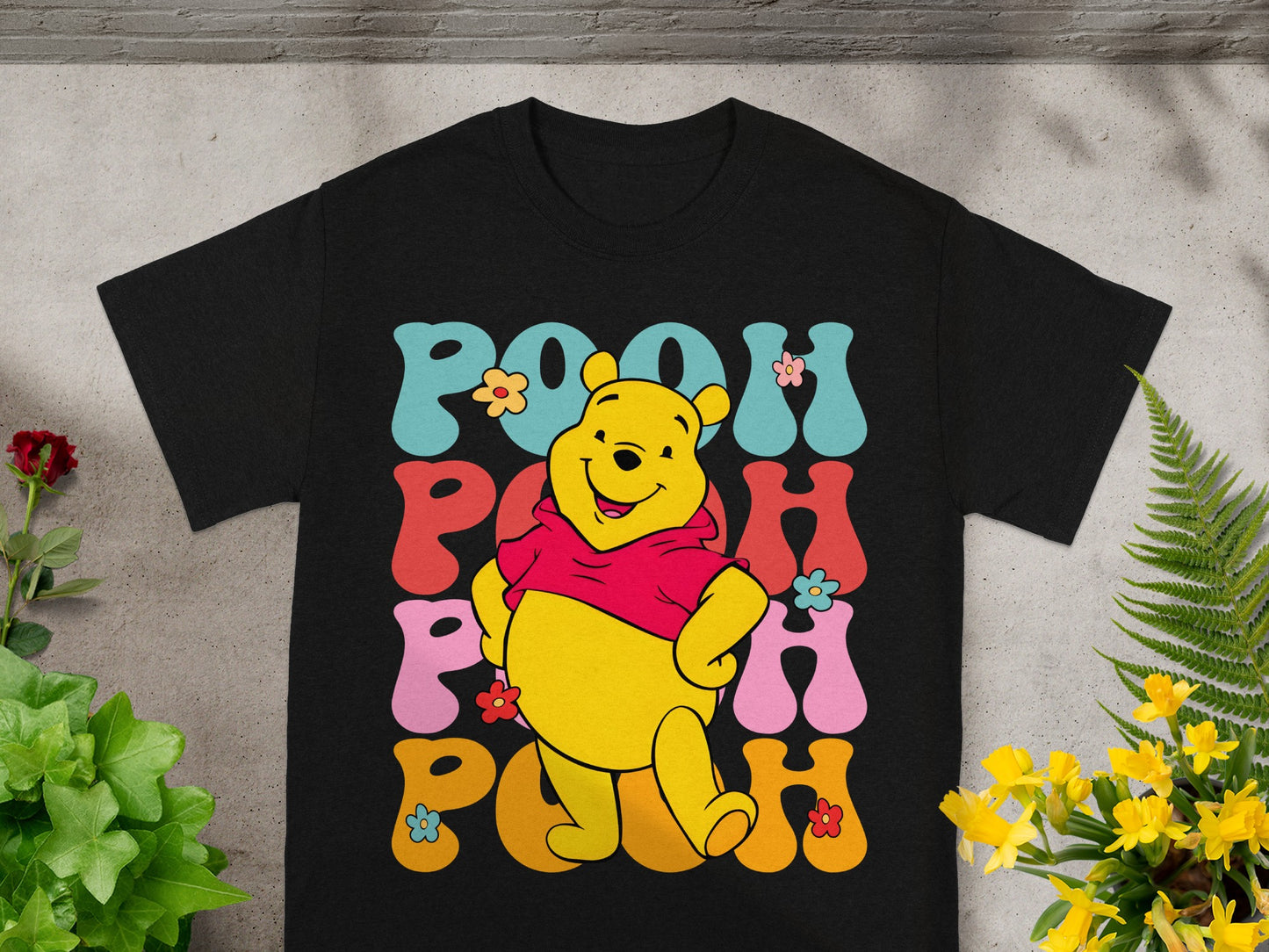 Black t-shirt with Winnie the Pooh and "POOH" text in colorful floral lettering.