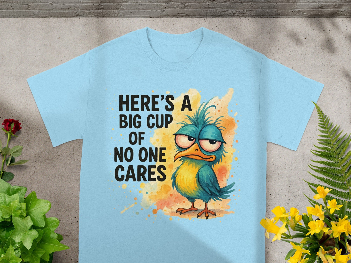 Light blue t-shirt with a cartoon bird graphic and text "Here's a big cup of no one cares".
